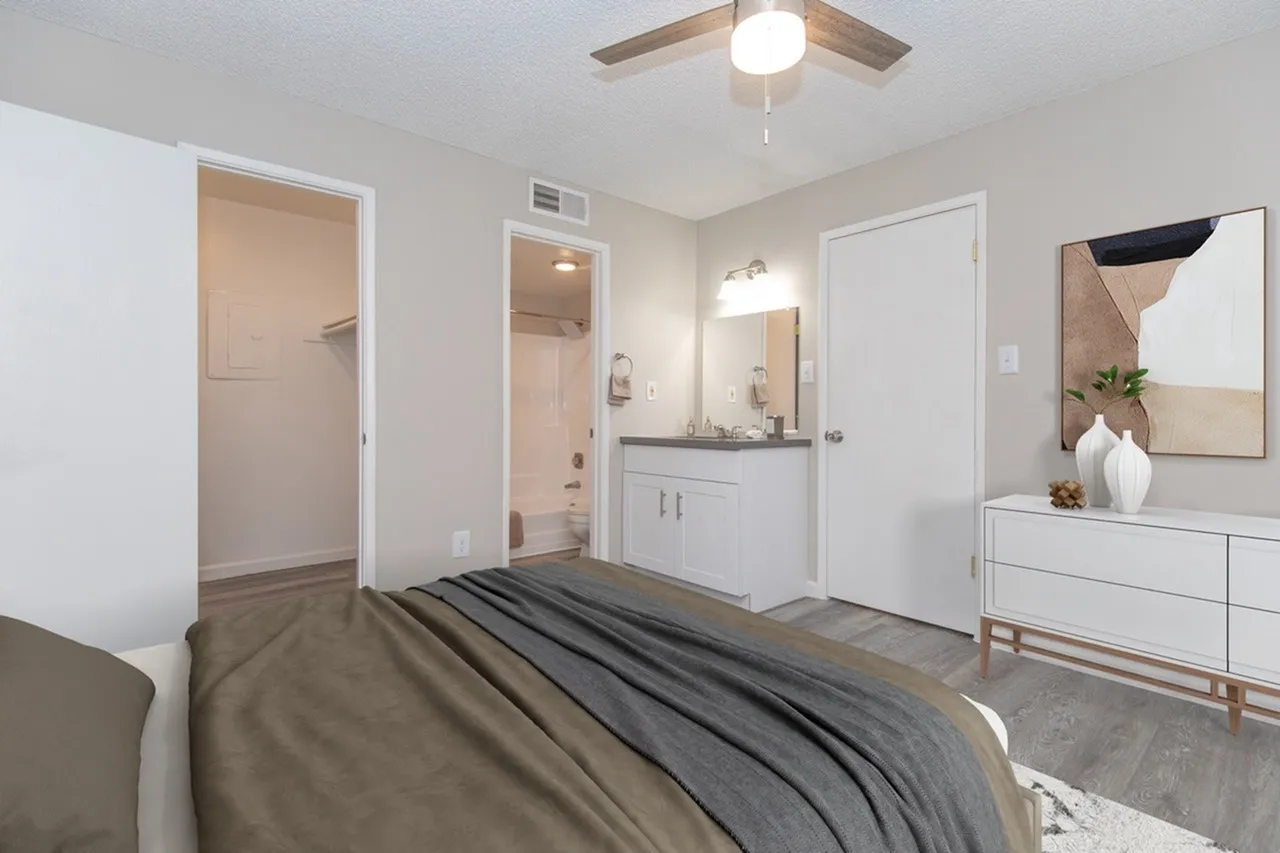 Primary bedroom, wood-style plank flooring, ceiling fan, white dresser, ensuite bathroom with vanity