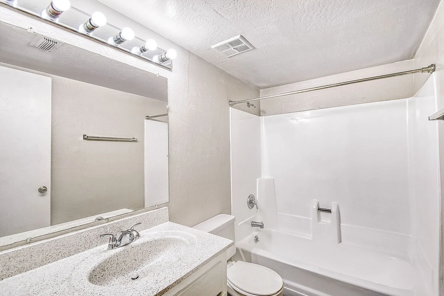 Bathroom, speckled quartz countertops, large mirror, white subway tile shower surround