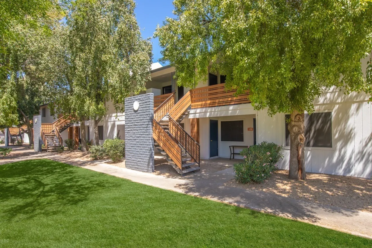 Exterior building with wood stairs, blue stone accent wall, green lawn, mature trees