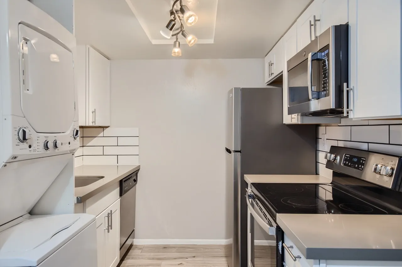 Galley kitchen, white shaker cabinetry, quartz countertops, stainless appliances, wood-style plank flooring