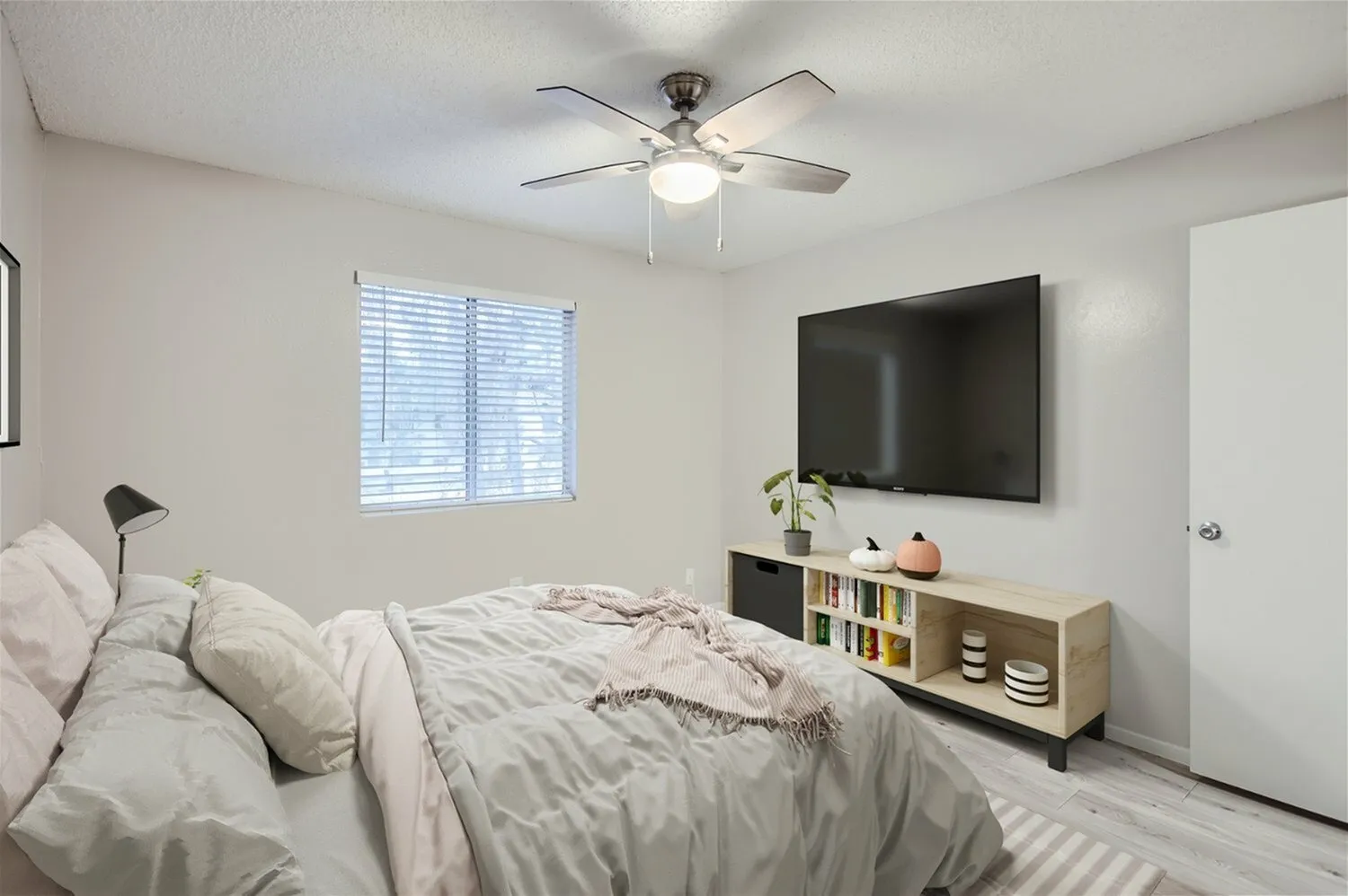 Primary bedroom, wood-style plank flooring, ceiling fan with light fixture, wall-mounted TV, storage shelving