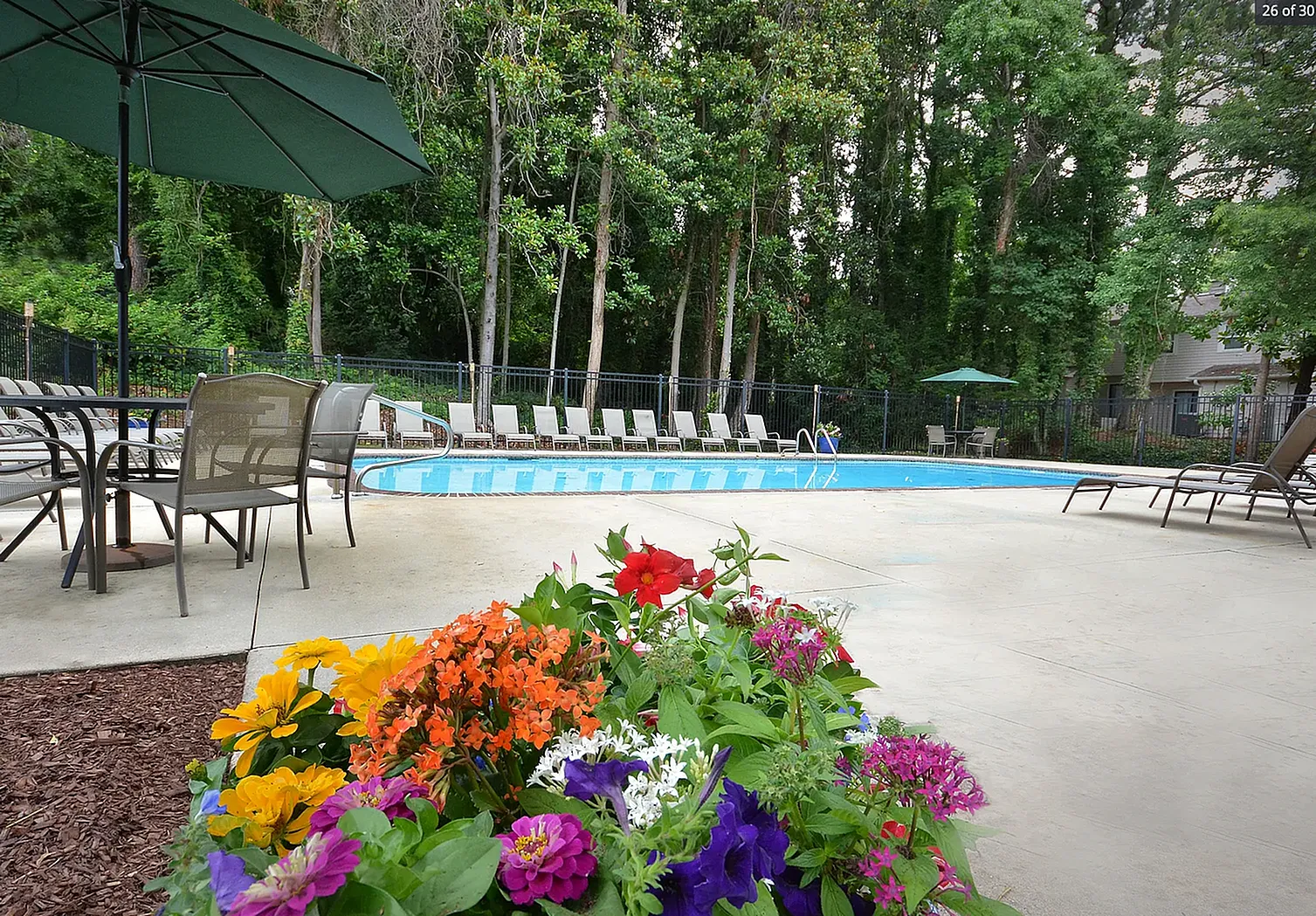 Resort-style pool, lounge chairs, umbrella, colorful flower garden, mature trees