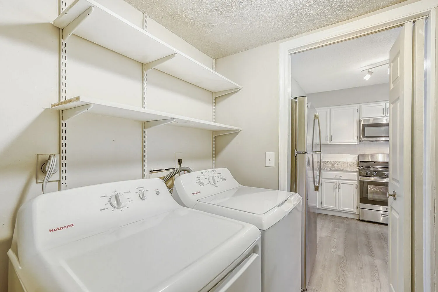 Laundry room, front-load washers and dryers, open shelving, kitchen visible through doorway