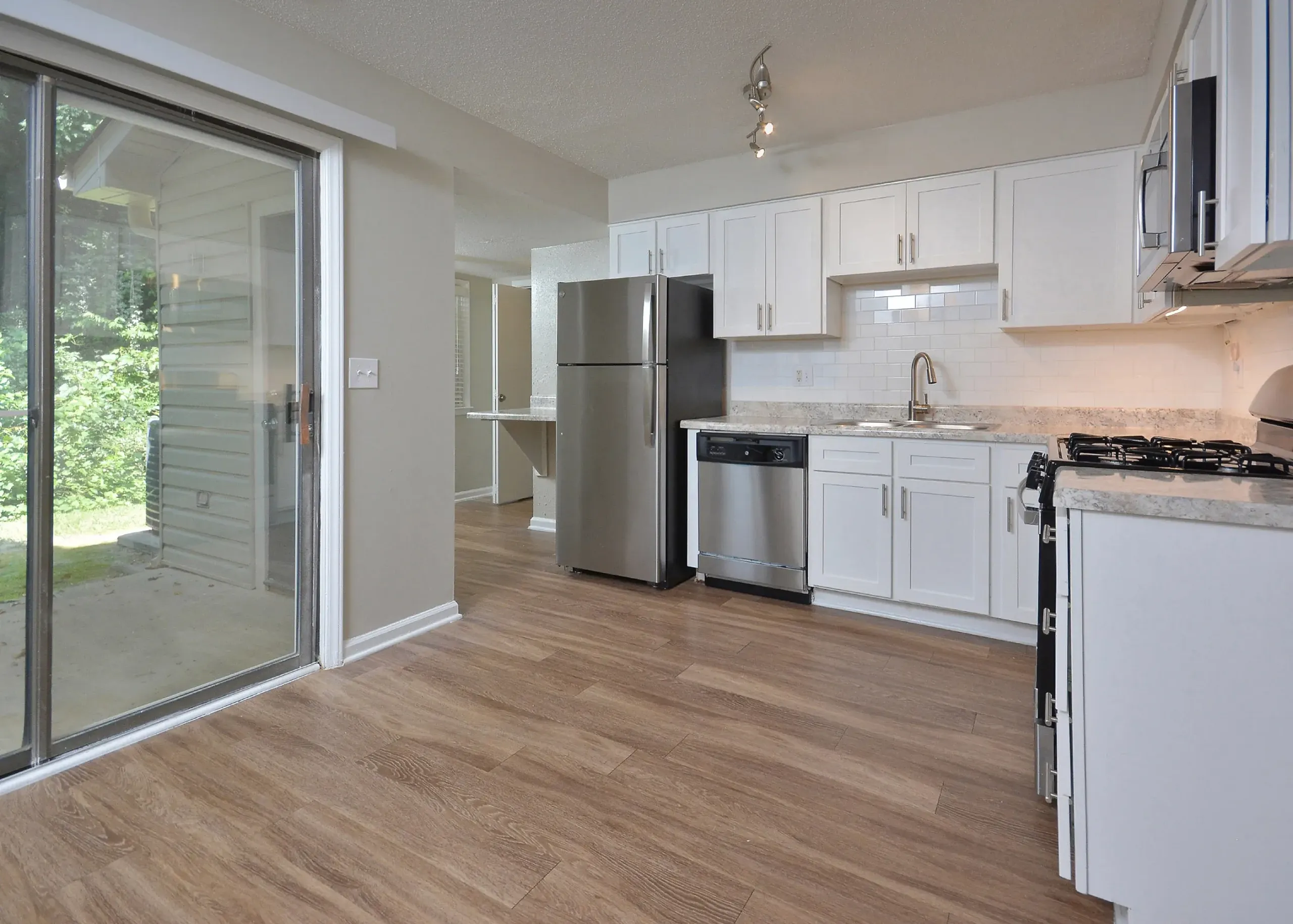 Kitchen with white shaker cabinetry, stainless steel appliances, quartz countertops, wood-style plank flooring, sliding glass door to patio