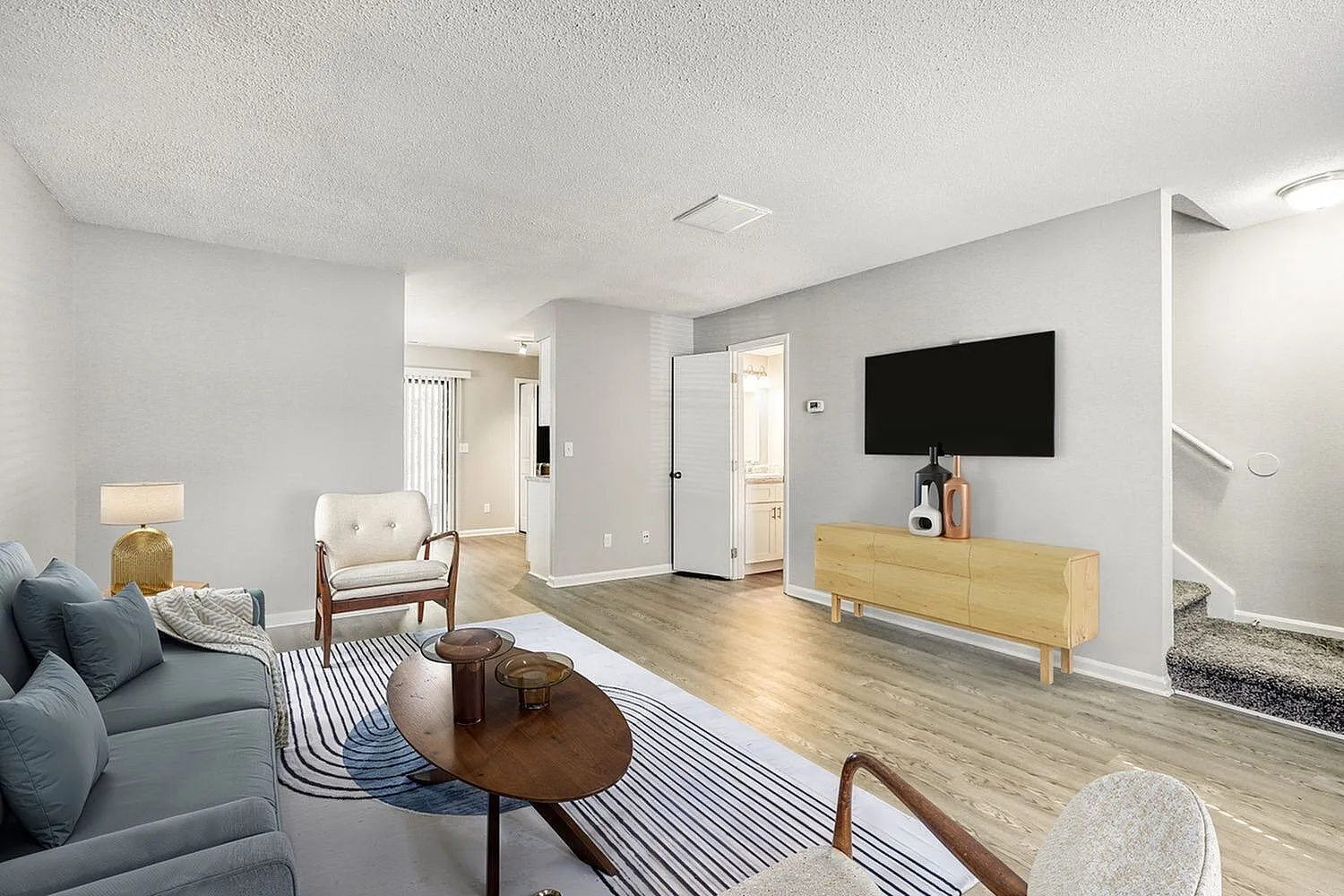 Living room, wood-style plank flooring, wall-mounted TV, cream armchair, round wood coffee table