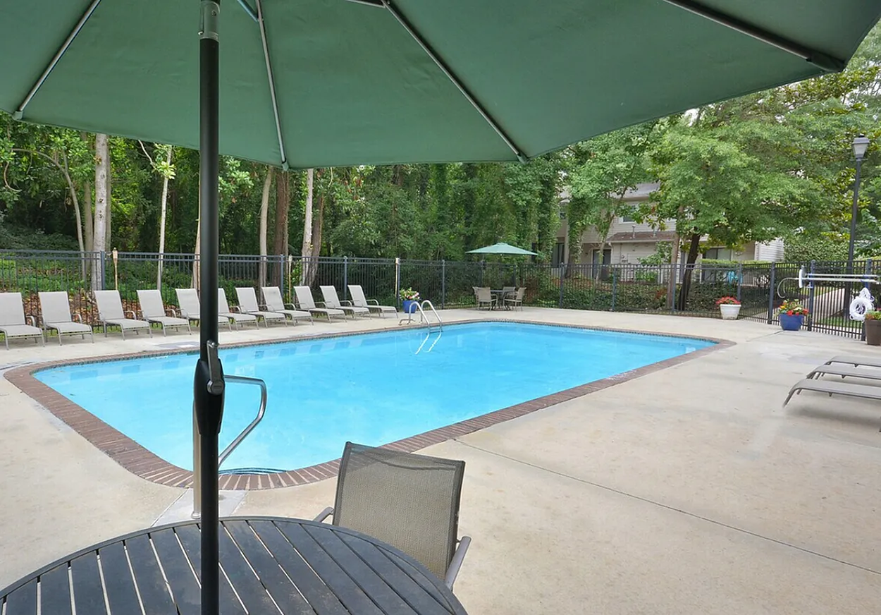 Resort-style swimming pool, lounge chairs, green umbrella shade structure, tree-lined grounds