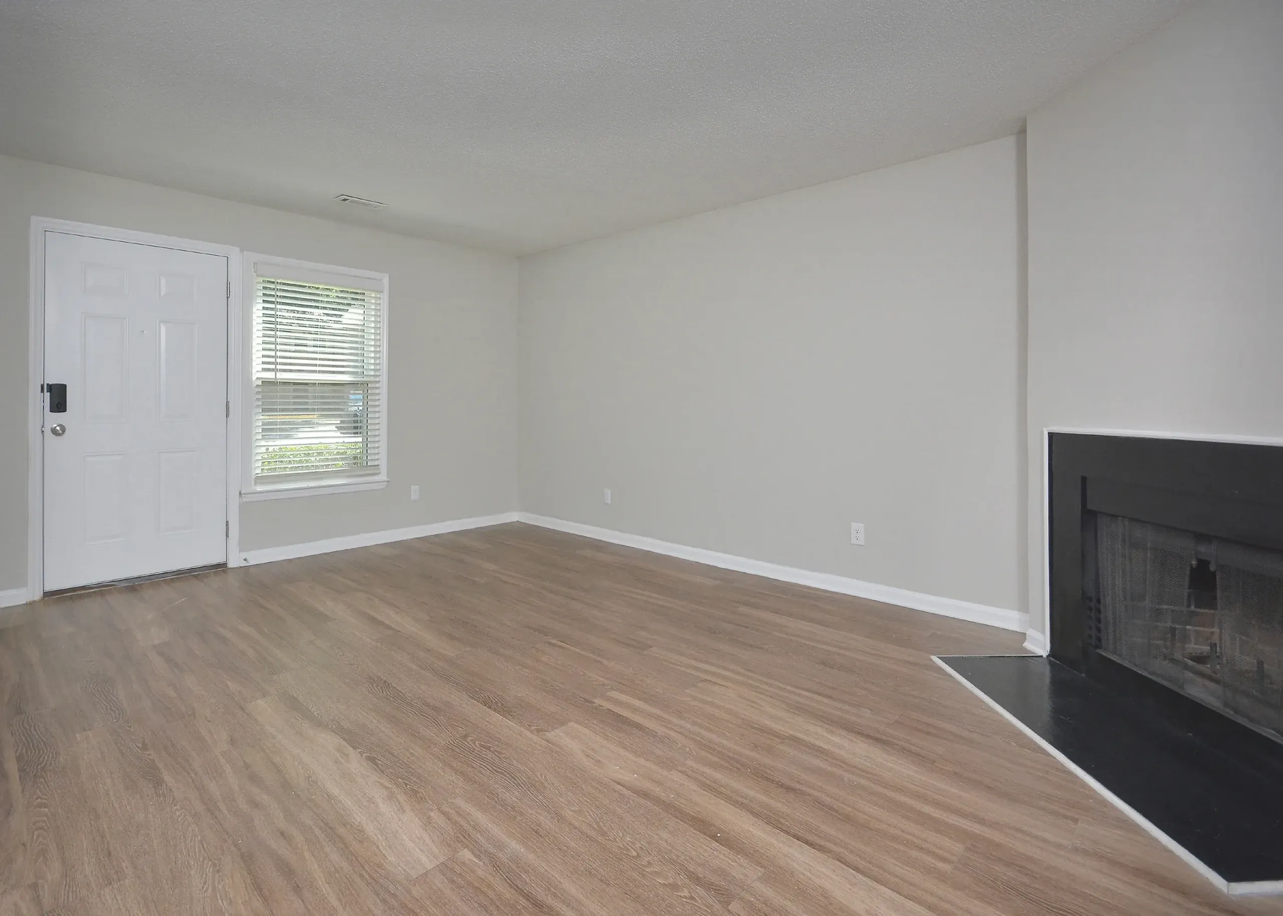 Living room with wood-style plank flooring, white walls, black fireplace, window with shutters
