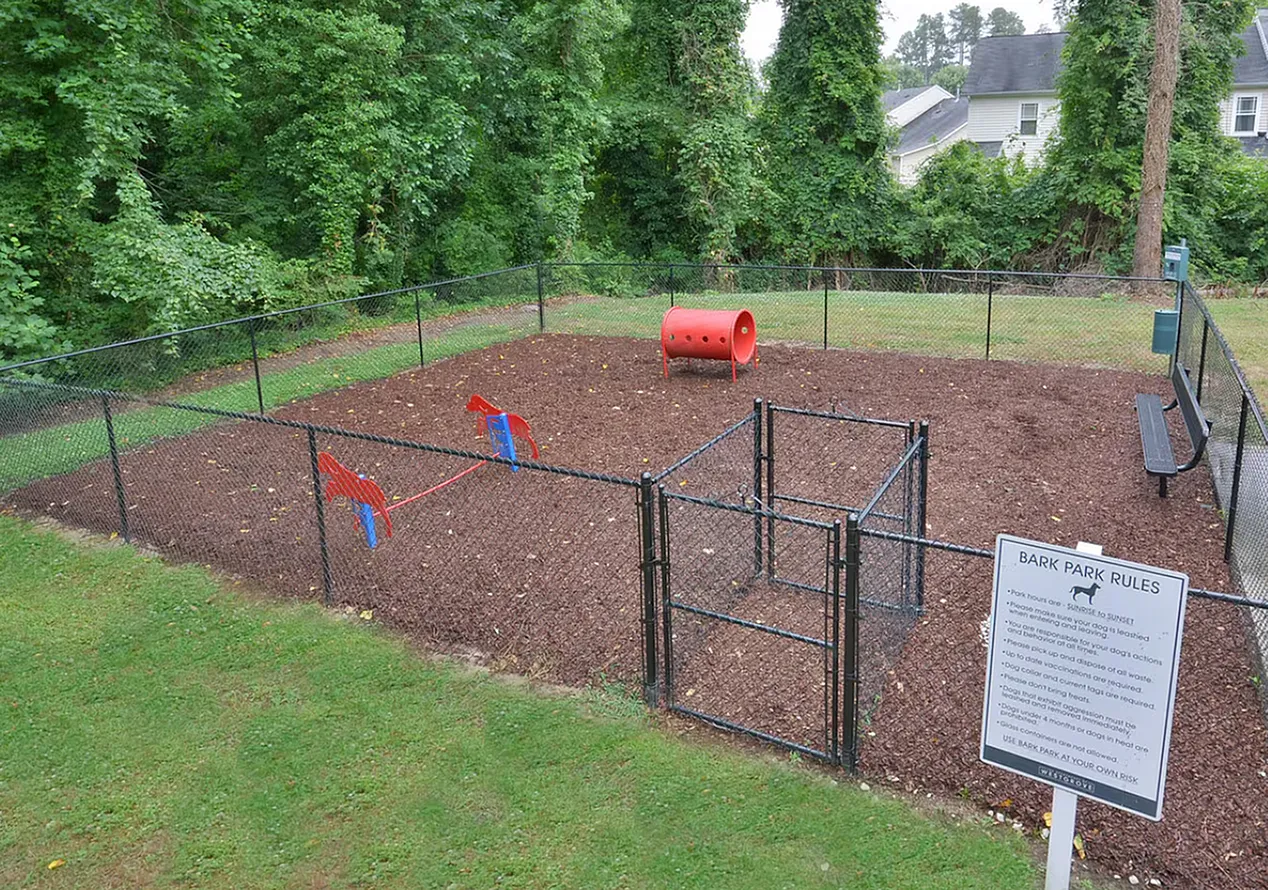 Dog park with fencing, red agility equipment, mulch ground, park rules sign