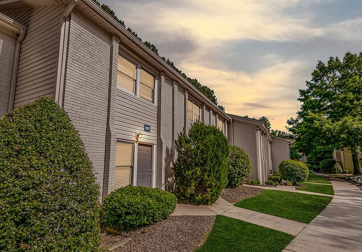 Apartment building exterior, brick facade, landscaped shrubs, modern entrance doors, driveway