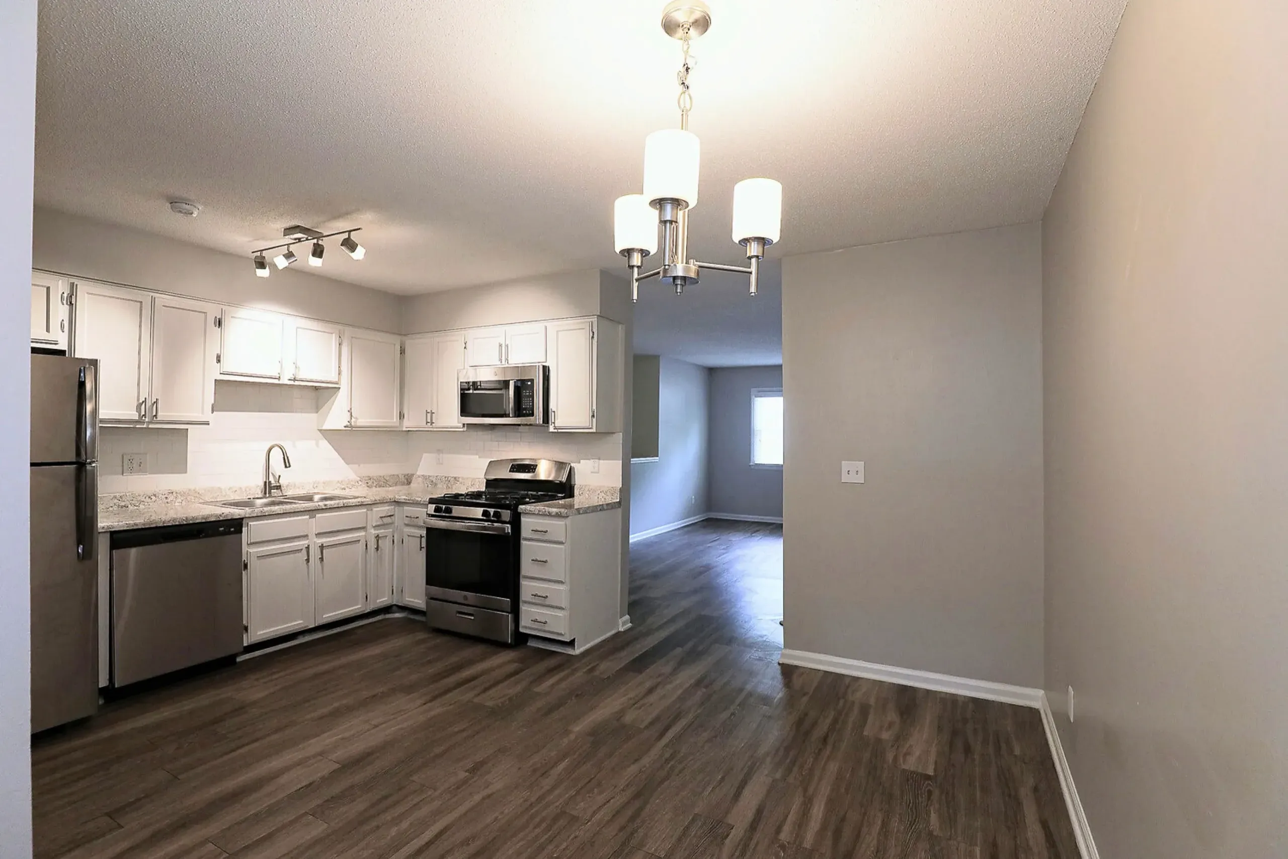 Kitchen with white shaker cabinetry, quartz countertops, stainless appliances, wood-style plank flooring, pendant lighting