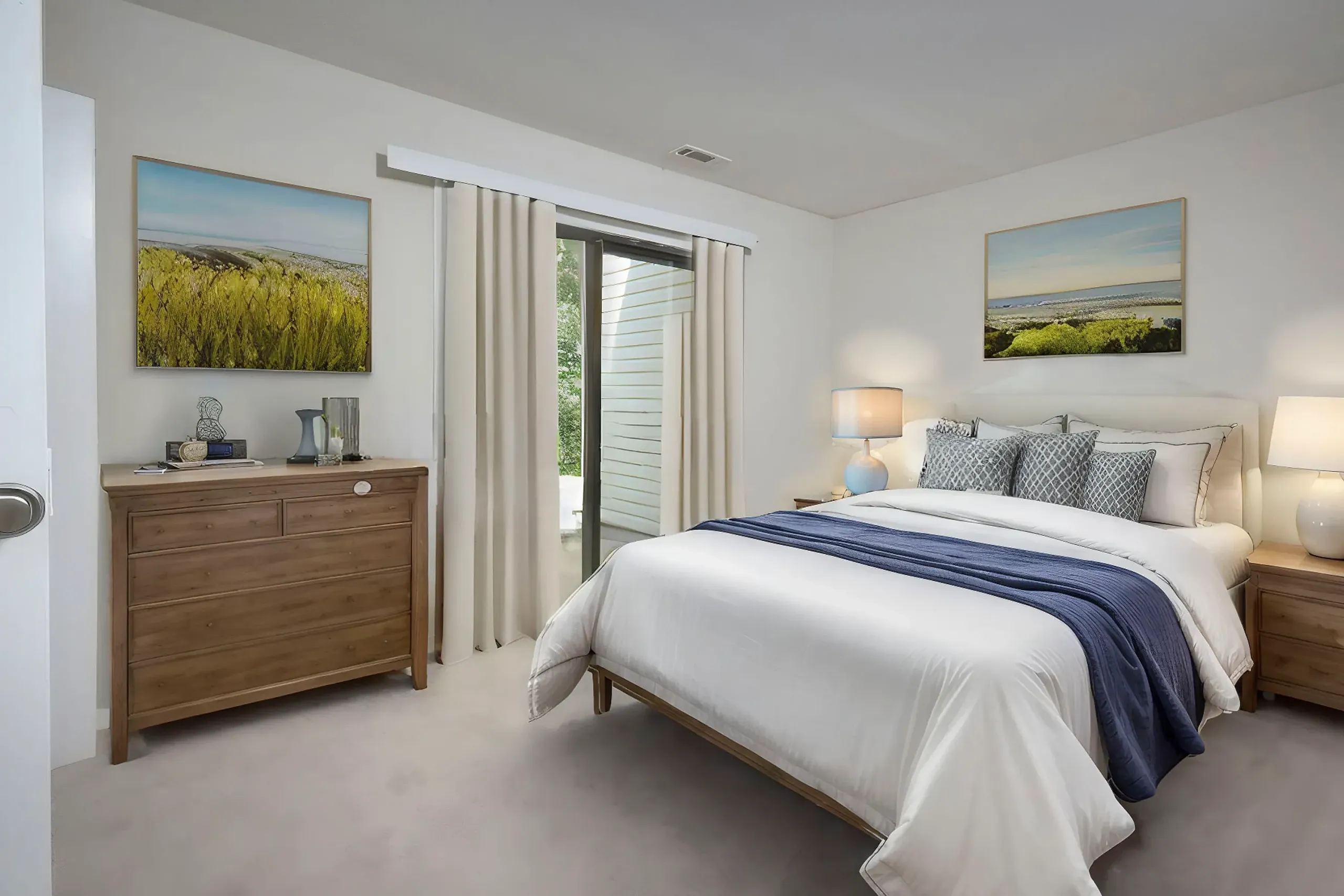 Primary bedroom, wood-style plank flooring, wood dresser, bed with blue throw, landscape artwork