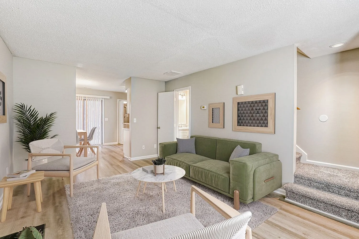 Living room with sage green sofa, wood-style plank flooring, round white coffee table, framed artwork, open entry to hallway