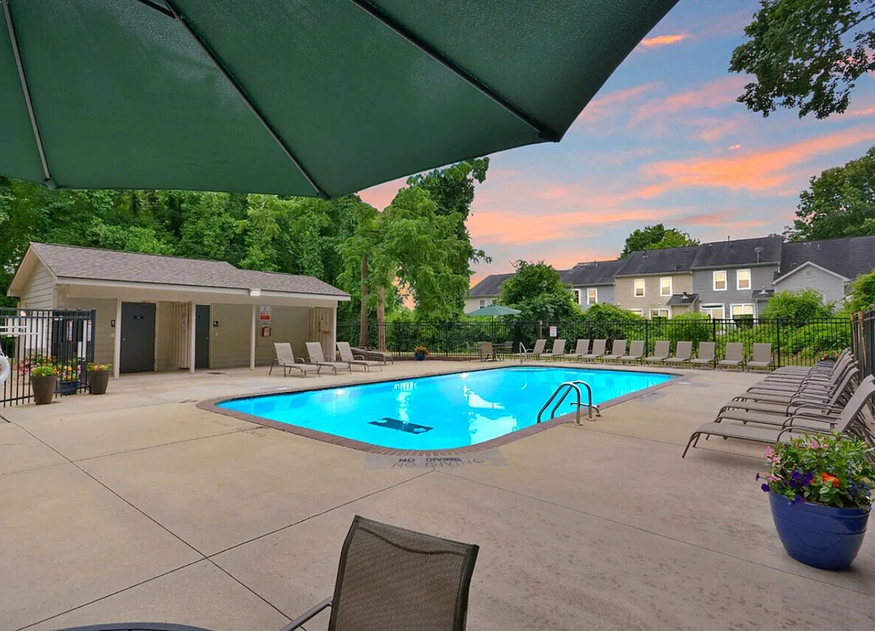 Community pool area, blue rectangular pool, loungers, green umbrella, pool house, residential buildings