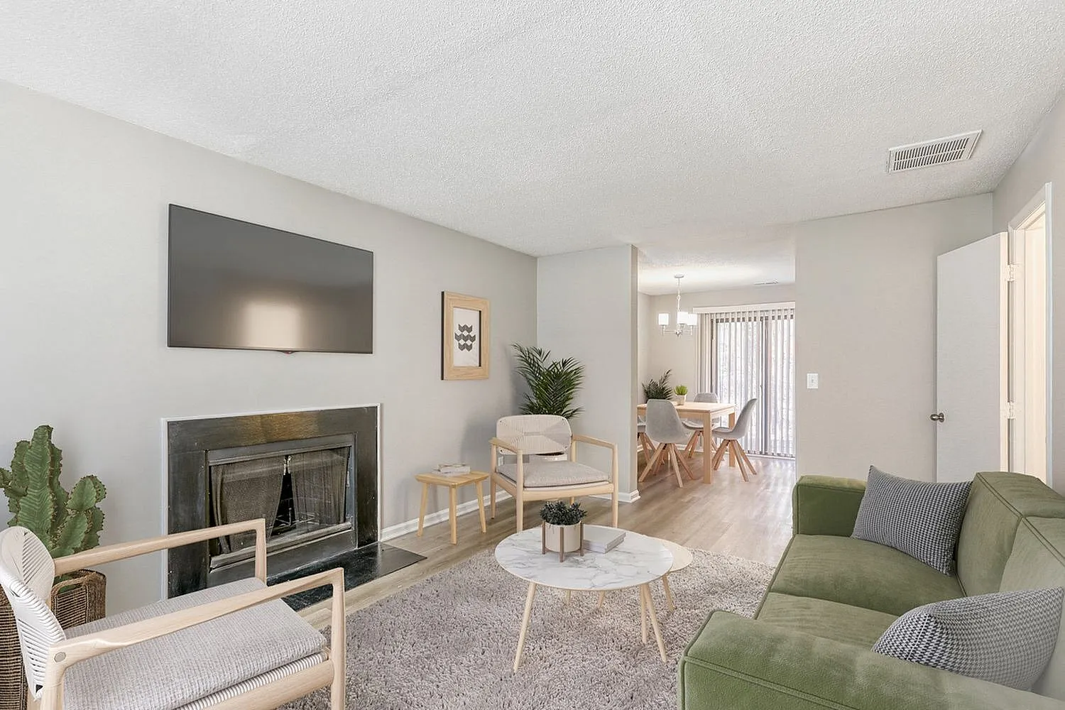 Living room, wood-style plank flooring, gray fireplace, wall-mounted TV, green upholstered seating